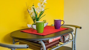 A table with a green mug, a purple mug, and a white orchid vase against a yellow wall.