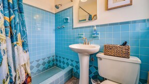 Un baño con baldosas azules, un lavamanos blanco, un inodoro, una ducha con puerta de cristal y una decoración de estrella de mar enmarcada en la pared.