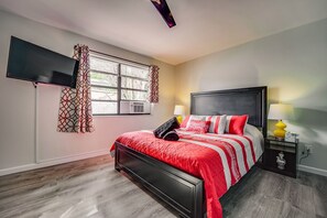 A bedroom with a bed, two bedside tables, a TV mounted on the wall, and a window with curtains. - 🏳️‍🌈 #7 Walk to Wilton Drive (Fort Lauderdale)