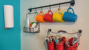 Una pared con un sujetapapeles higiénicos, un juego de tazas de colores, un recipiente con servilletas de papel y un portalapices.