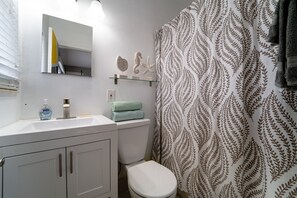 Bathroom features a sink, mirror, toilet, and shower with a fern-patterned curtain.