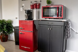 Compact kitchenette with a refrigerator, microwave, and coffee maker, plus a potted plant for a touch of greenery.
