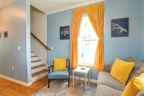 Ein Wohnzimmer mit Treppe, einem blauen Sofa inklusive gelber Kissen, einem kleinen Tisch und zwei Wandbildern von Walen.