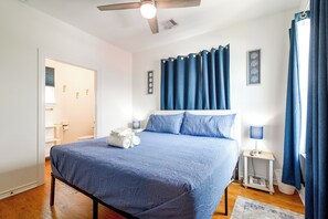 A bedroom with a bed, a nightstand, a lamp, a ceiling fan, and a bathroom door.