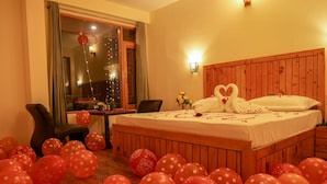 A hotel room with a wooden headboard, a bed with white linens, and red balloons scattered on the floor. - Hotel Ireland (Manali)