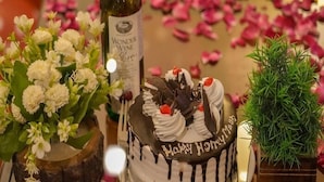 A cake with "Happy Anniversary" written on it, surrounded by flowers and a bottle of wine. - Hotel Ireland (Manali)