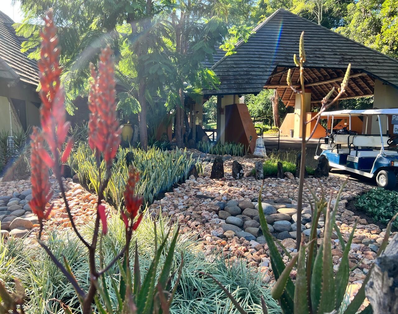 Un jardin agrémenté d’un belvédère, un chariot de golf garé et un bâtiment doté d’un toit en tuiles.
