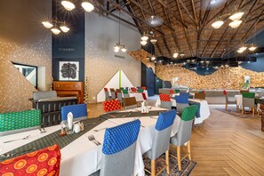 Un restaurant avec des tables rondes, des chaises et un plafond haut avec des poutres apparentes.