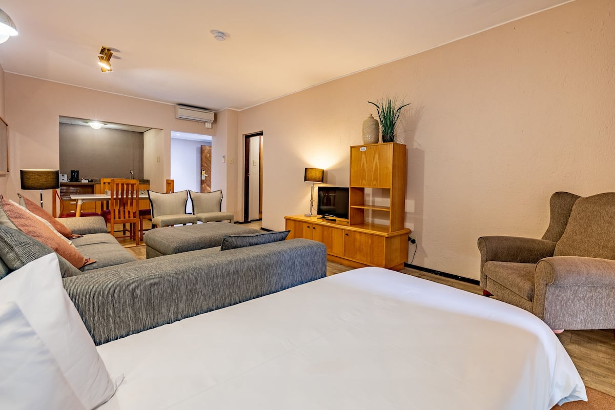 Una habitación de hotel con una cama grande, un sofá, un mueble de madera con un televisor y una silla.