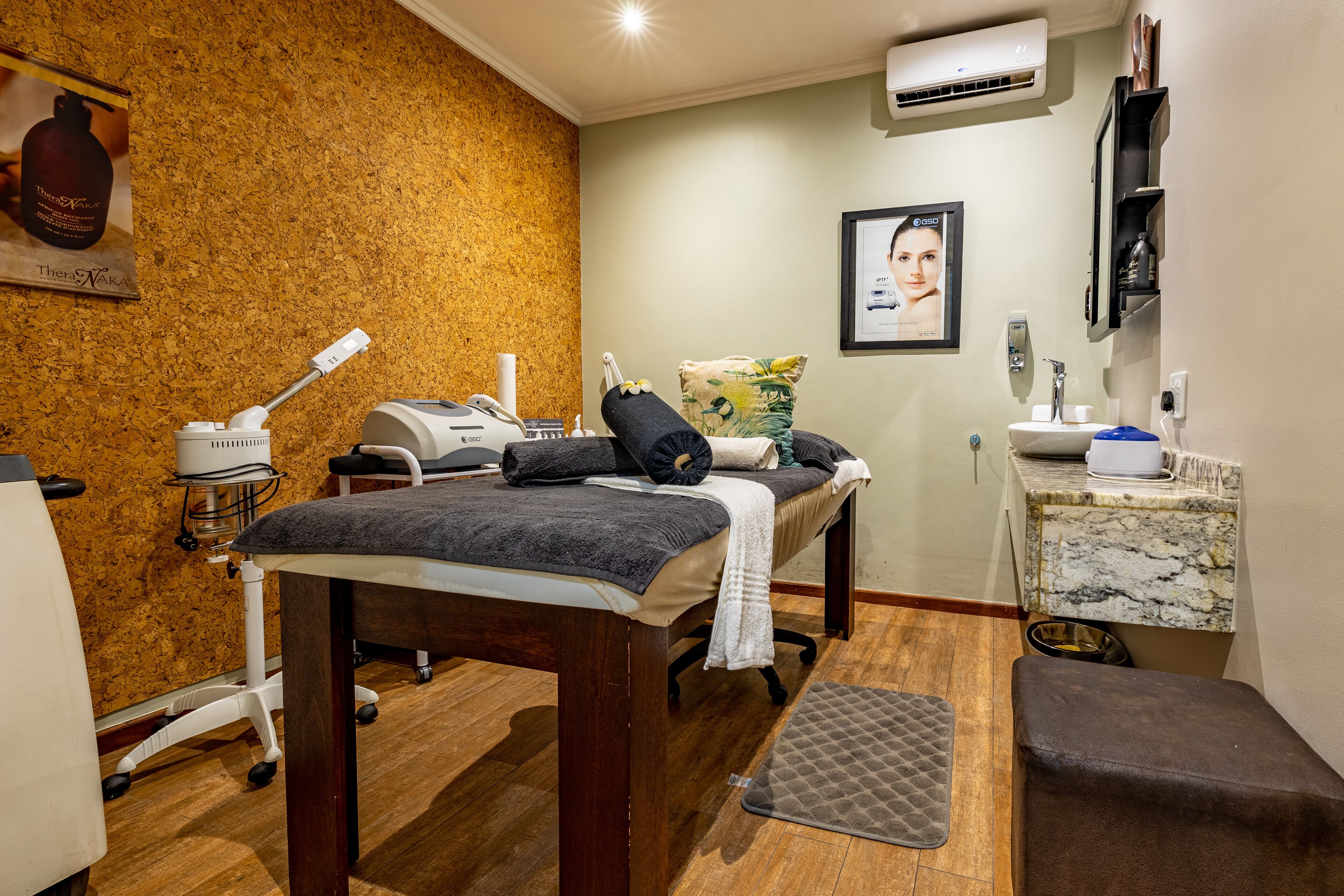 Ein Spa-Raum mit Massagetisch, einem kleinen Waschbecken und einem Spiegel.