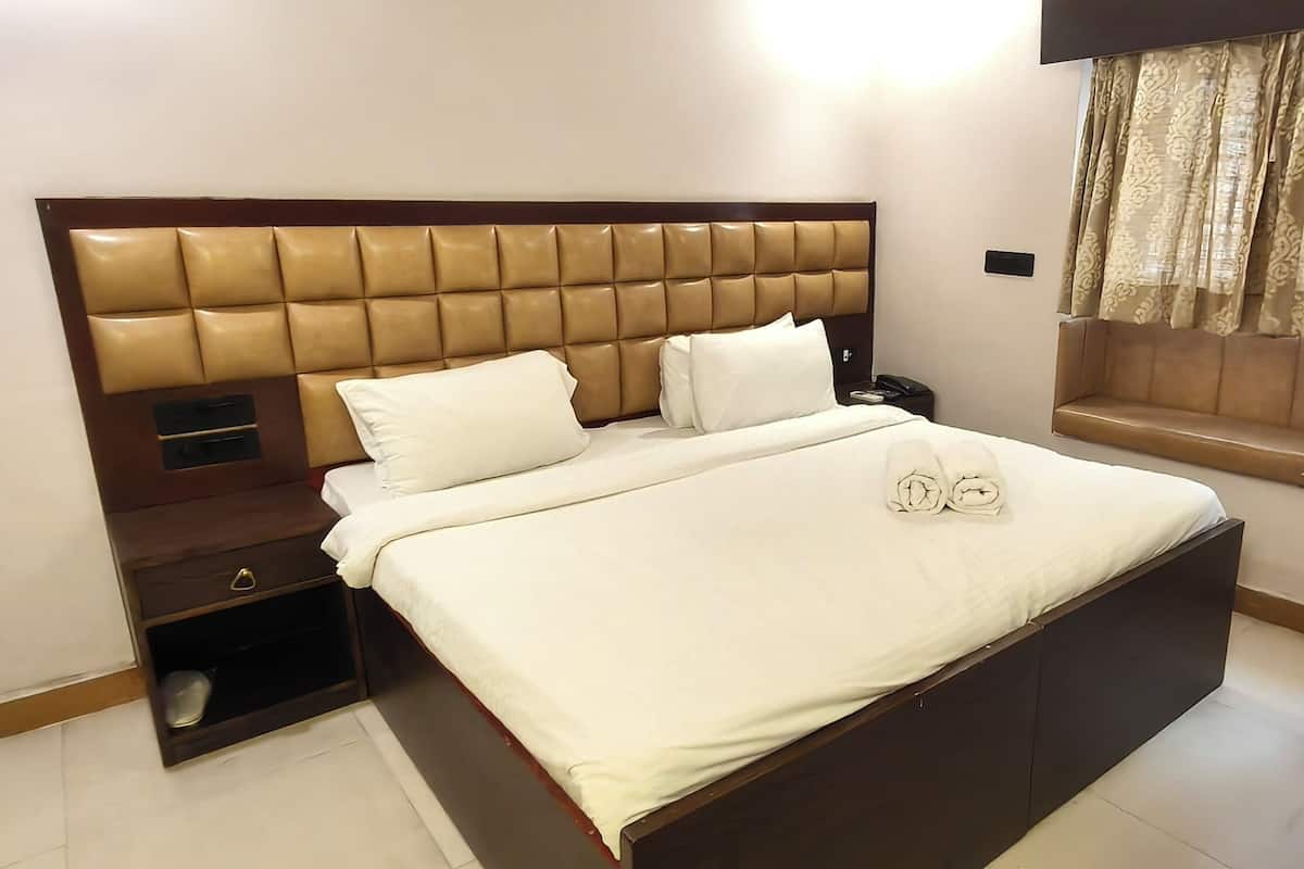Une chambre d’hôtel moderne avec un grand lit, une table de chevet, une commode et une fenêtre avec des rideaux.