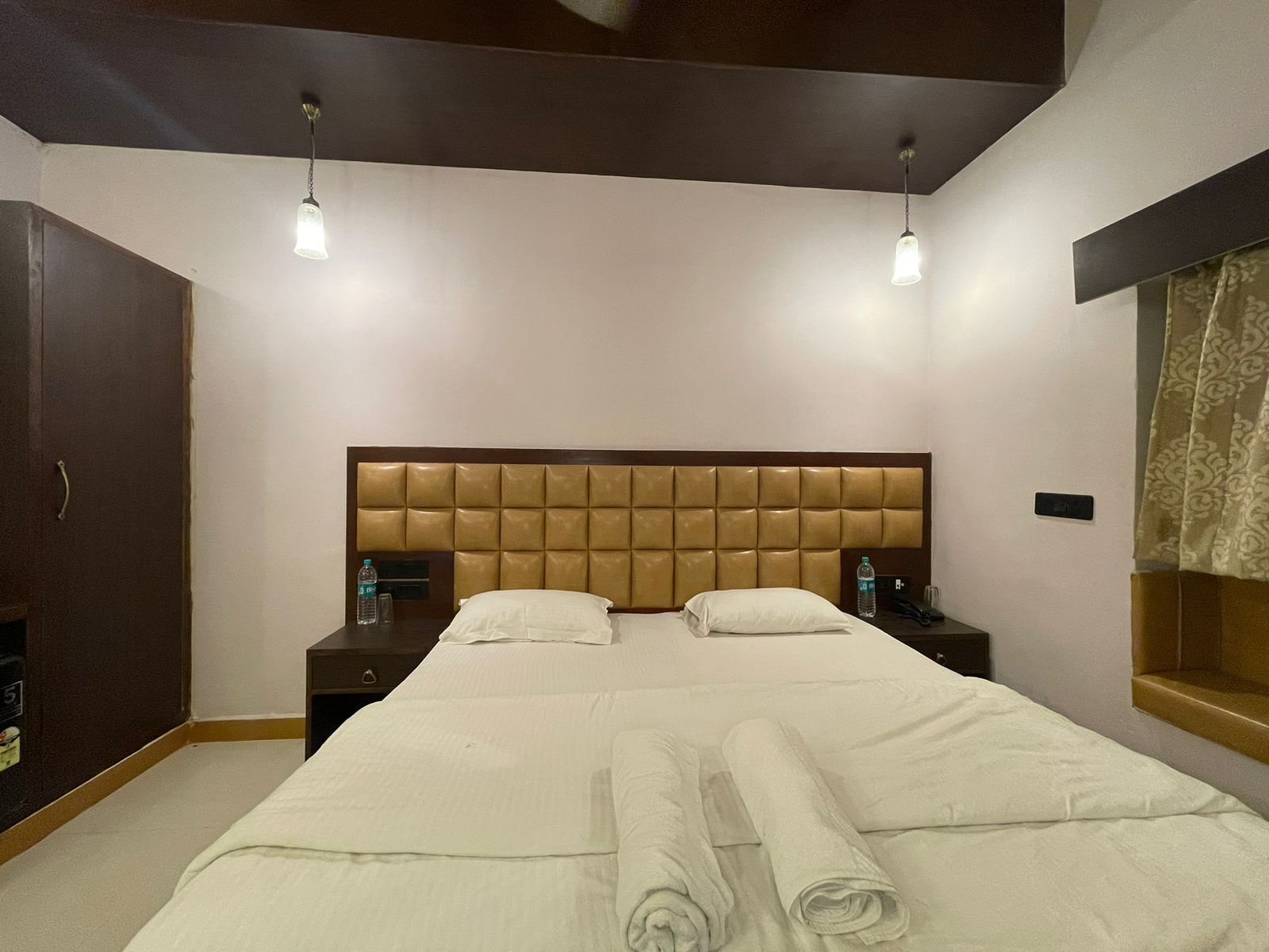 Una habitación de hotel con una cama grande, dos mesitas de noche, un armario y una ventana con cortinas.