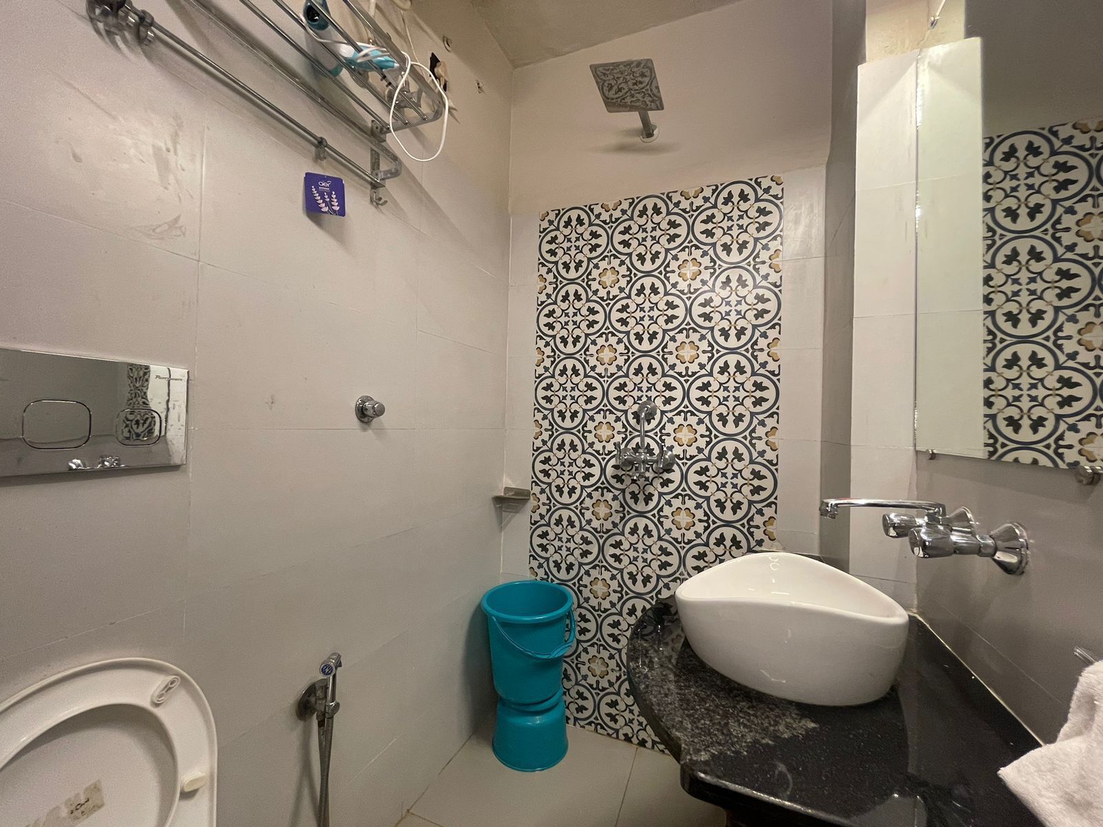 A bathroom with a white toilet, a sink with a black countertop, a shower, and a patterned tile wall.