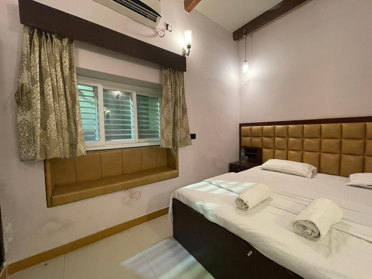 A hotel room with a bed, a window with curtains, a bedside table, and a headboard.