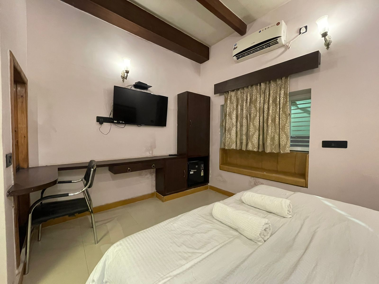 Une chambre d’hôtel comprenant un lit, un bureau avec une chaise, un téléviseur fixé au mur et un appareil de climatisation.