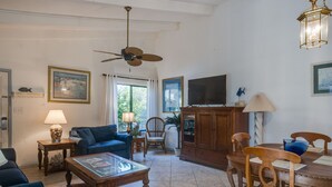 A living room with a television, a ceiling fan, a dining table with chairs, a sofa, and a coffee table.