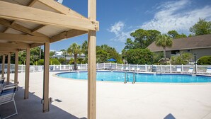 A pool area with a wooden pergola, lounge chairs, and a fenced swimming pool.