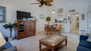 A spacious living room with a television, wooden cabinet, dining table, and chairs.