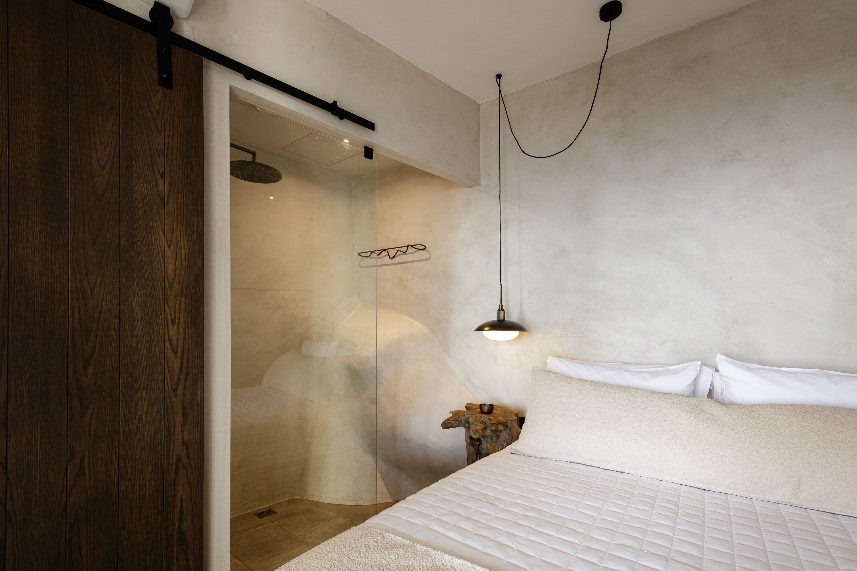 A bedroom with a bed, a wooden wardrobe, a hanging light fixture, and a shower area.