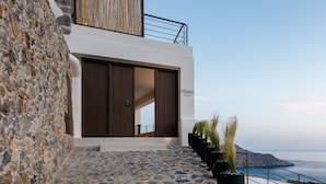 A modern building with a stone facade, a wooden door, and a balcony overlooking the sea. - Fedra Suites (Agios Vasileios)