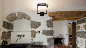 A stone-walled bathroom with a sink and a wall-mounted light fixture. - Fedra Suites (Agios Vasileios)