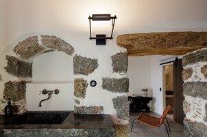 Baño con paredes de piedra, un lavamanos y un aplique de pared.