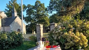 A picnic setup with a table, a teapot, and a blanket in a garden with a stone building in the background. - Gîte** 13 beds, sleeps 20, Jacuzzi, Swimming pool, Billiards, Games tent, Park **. (Mohon)