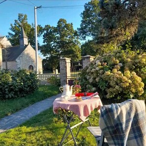 Enjoy a serene outdoor dining experience amidst lush greenery and a historic stone building.