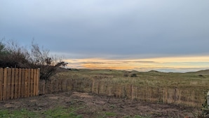 Un espacio al aire libre cercado, con suelo de tierra y poca hierba, rodeado de colinas y un cielo nublado.