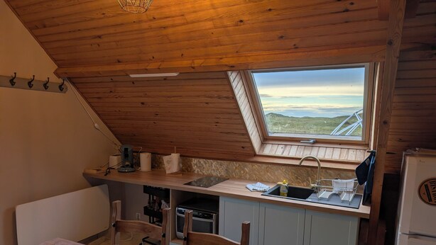 Una cocina acogedora con techo de madera, tragaluz, mesa de madera y vistas al campo.