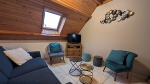 Una sala de estar estilo loft acogedora, con techo inclinado, televisor, sofá, sillón y una pequeña mesita.