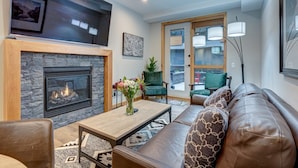 A living room with a fireplace, a sofa, a coffee table with flowers, and a view through a glass door.