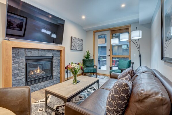 A living room with a fireplace, a sofa, a coffee table with flowers, and a view through a glass door.