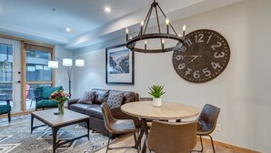 A modern living room with a round table, brown leather chairs, a large wall clock, and a chandelier.