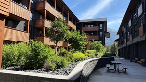 A modern building with multiple balconies, a landscaped garden with various plants, and a paved walkway with benches.