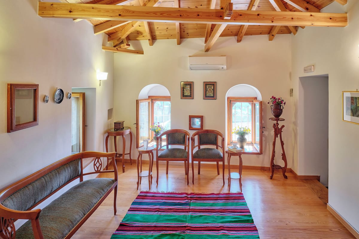 Um quarto espaçoso com vigas de madeira no teto, uma janela grande e um tapete colorido.