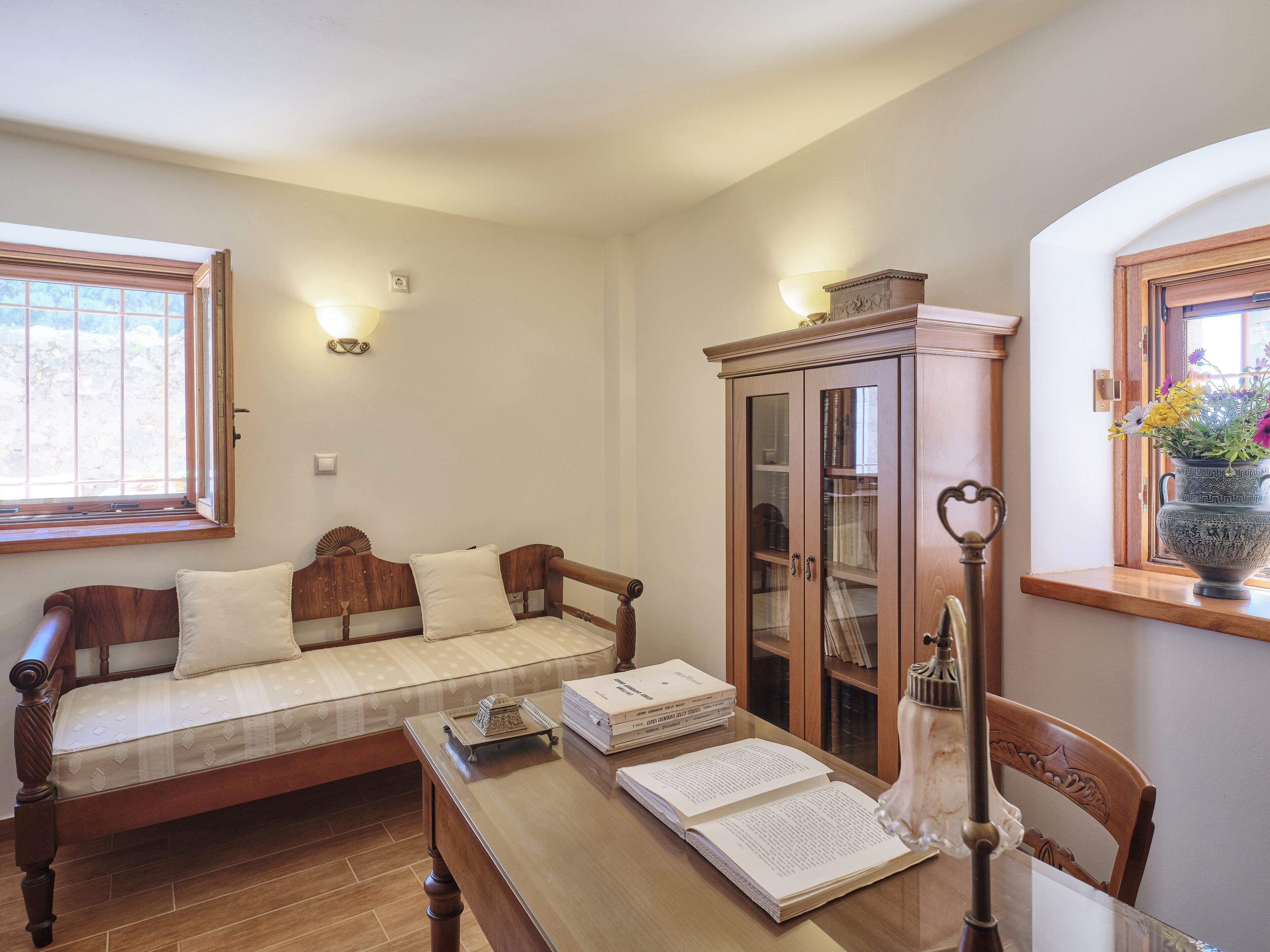 Una habitación acogedora con un sofá de madera, un aparador de madera con puertas de cristal y una mesa con libros y una lámpara.