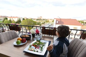 Un balcón con una mesa dispuesta para una comida, con vistas a un paisaje urbano que incluye edificios y una iglesia.