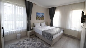 A bedroom with a large bed, a nightstand, a waste basket, and a painting on the wall. - Trigo Hotel (Nevsehir)