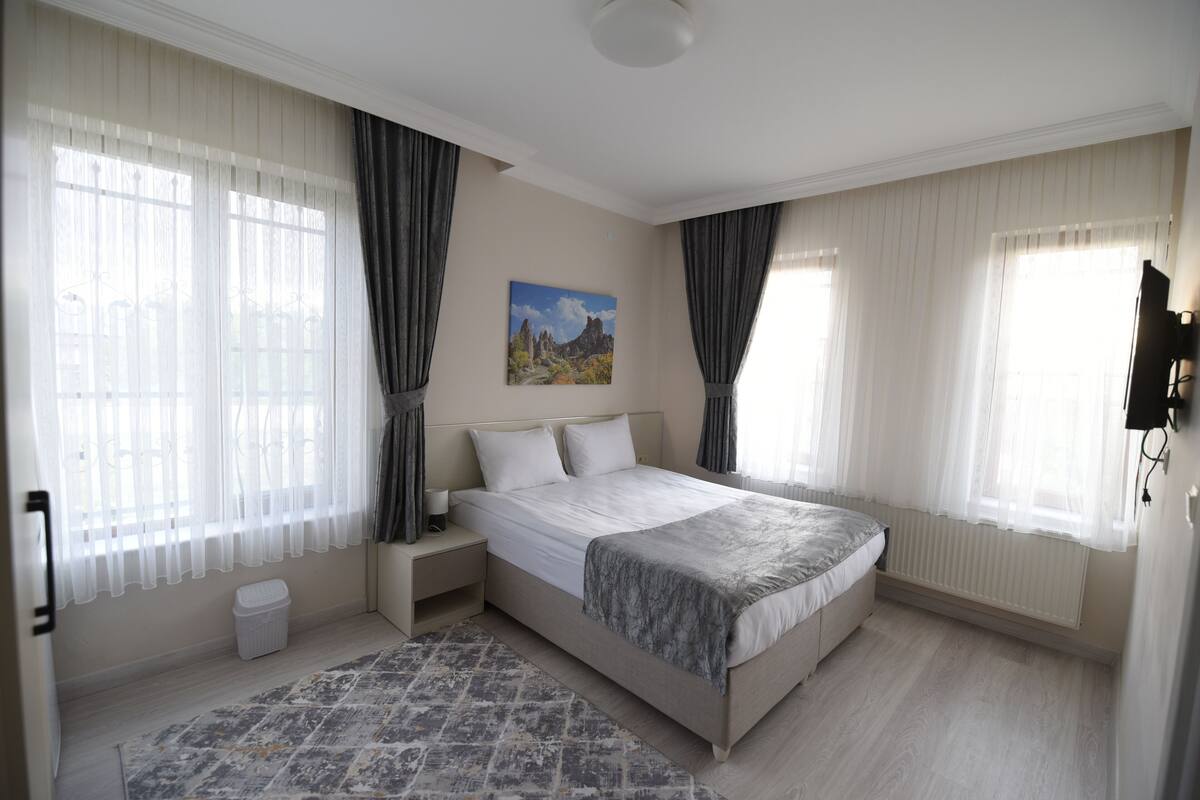 A bedroom with a large bed, a nightstand, a waste basket, and a painting on the wall.