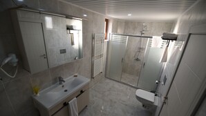 A modern bathroom with a sink, mirror, towel rack, shower, and toilet. - Trigo Hotel (Nevsehir)
