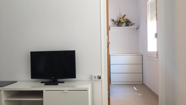 A room with a TV on a white desk, a white wardrobe, and a shelf with decorative items. - CENTRAL AND RENOVATED APARTMENT, 100m FROM THE BEACH (Torroella de Montgrí)