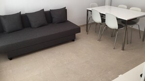 A modern living room with a dark grey sofa, a white dining table, and four white chairs. - CENTRAL AND RENOVATED APARTMENT, 100m FROM THE BEACH (Torroella de Montgrí)
