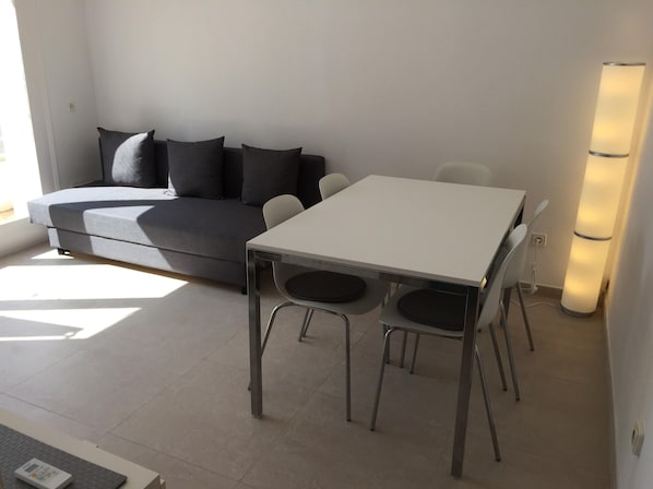 A modern living room with a grey sofa, a white dining table, and two chairs.