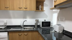 A modern kitchen with wooden cabinets, a stainless steel sink, a microwave, a toaster, and a dish rack. - CENTRAL AND RENOVATED APARTMENT, 100m FROM THE BEACH (Torroella de Montgrí)