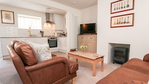 A modern living room with a brown leather sofa, a wooden coffee table, and a television. - Bay Cottage No 5 (Morecambe)