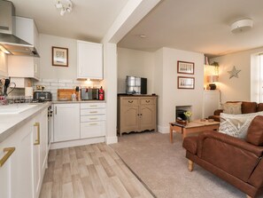 A modern kitchen with white cabinets, a dining area with a brown leather sofa, and a fireplace. - Bay Cottage No 5 (Morecambe)