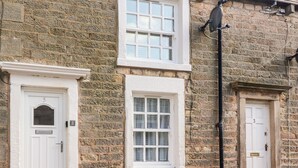 A stone building with three white doors, numbered 5, 3, and 7, and a window with white framing. - Bay Cottage No 5 (Morecambe)