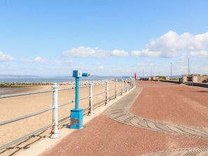 A coastal walkway with a metal railing, a blue structure, and a sandy beach. - Bay Cottage No 5 (Morecambe)