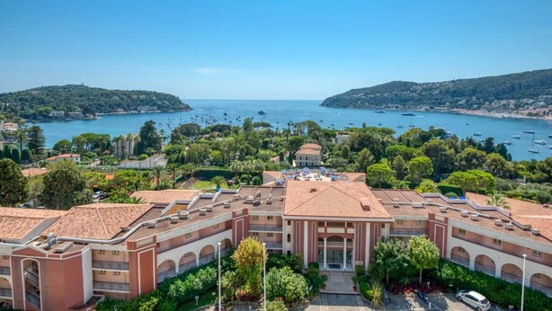 Un hotel costero con un patio central, varios balcones y vistas al mar y a los barcos.